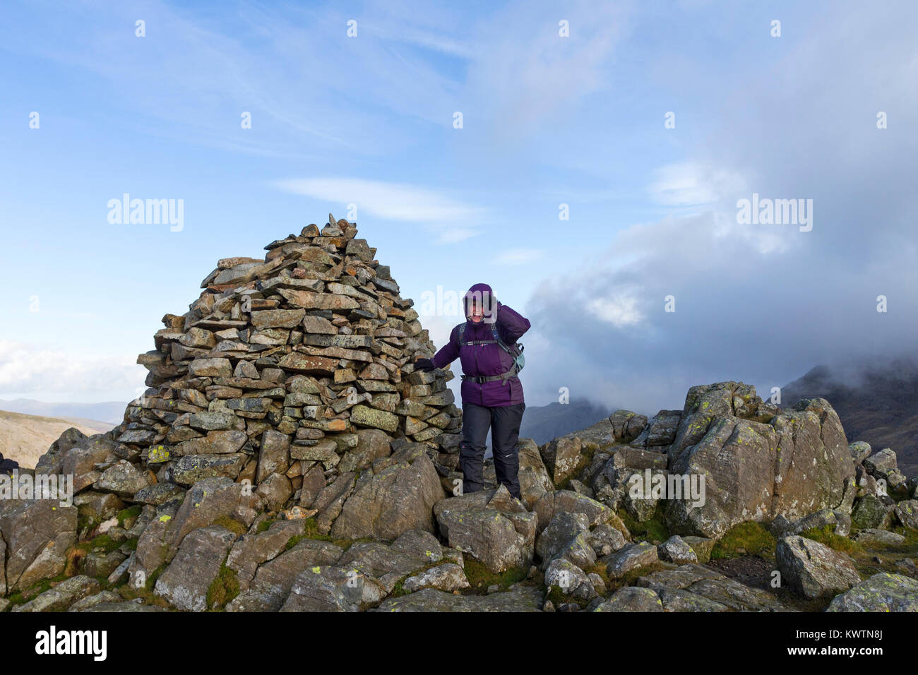 Laughing Middle Aged Walker Enjoying the Moment as Strong Winds Race Past the Summit Cairn of Lingmell, Lake District, Cumbria, UK. Stock Photo