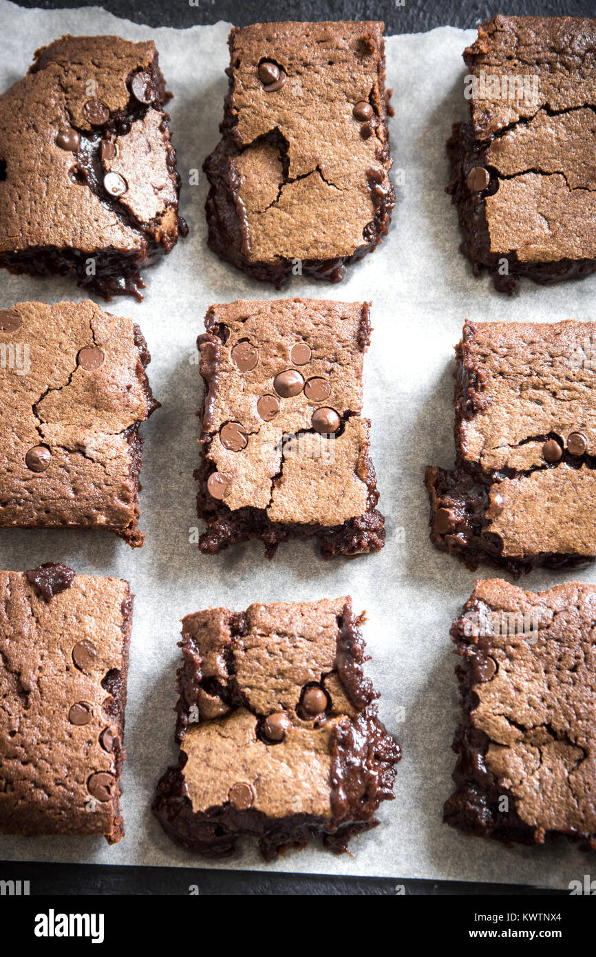 Double Chocolate Brownies. Homemade chocolate fudge brownies with chocolate chips on baking paper and black background. Stock Photo