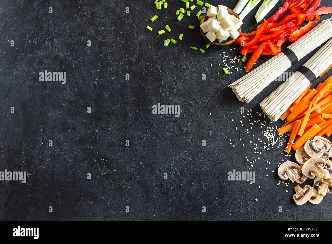 Vegetarian cooking ingredients for stir fry with tofu, noodles and vegetables. Asian vegan cuisine ingredients over black stone background with copy s Stock Photo