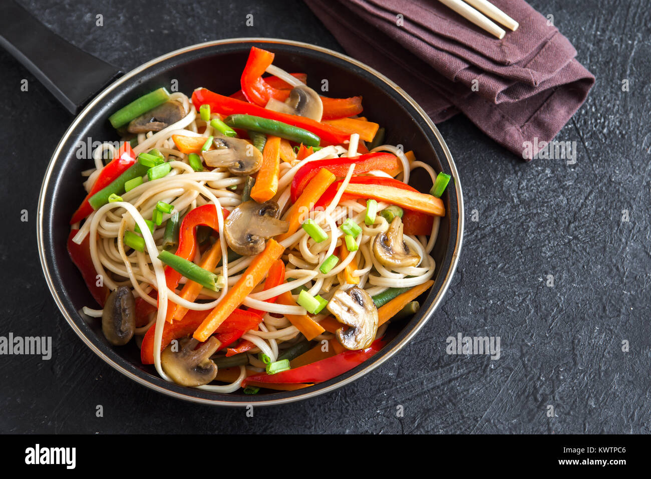 Stir fry with udon noodles, mushrooms and vegetables. Asian vegan vegetarian food, meal, stir fry over black background, copy space. Stock Photo