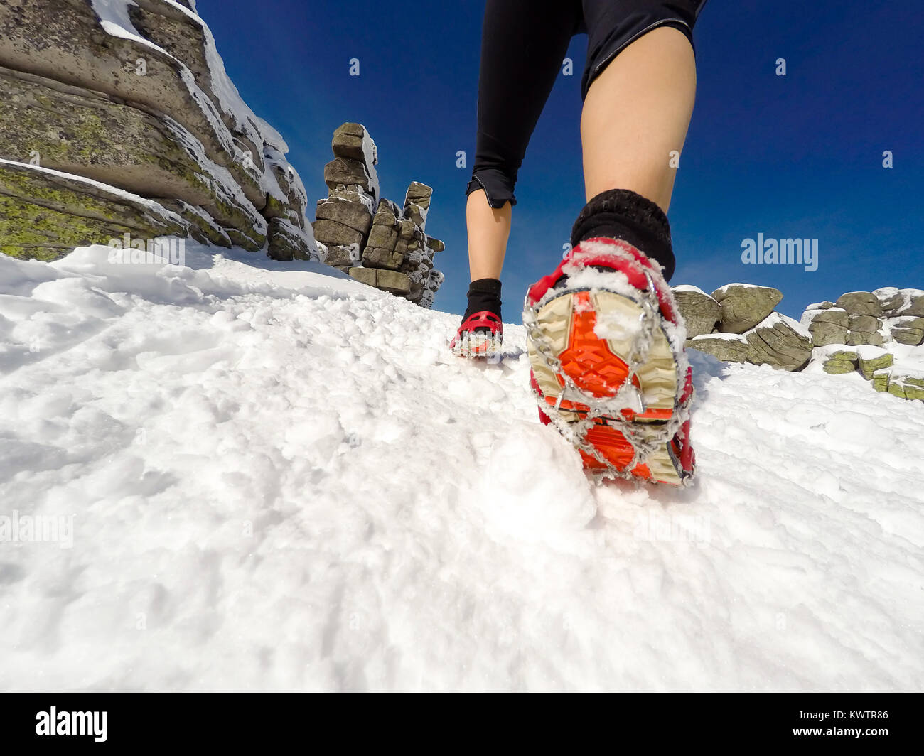 Running woman on winter trail, snow and white mountains. Young happy girl with backpack cross country running in mountains. Female trail runner joggin Stock Photo