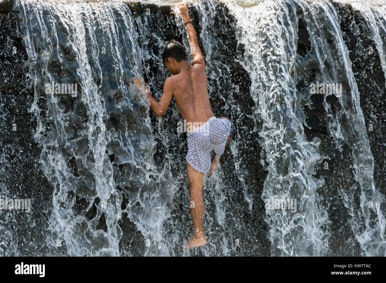 Youth climbing up the water cascade over the Tukad Unda Dam, Semarapura, Bali Island, Indonesia Stock Photo