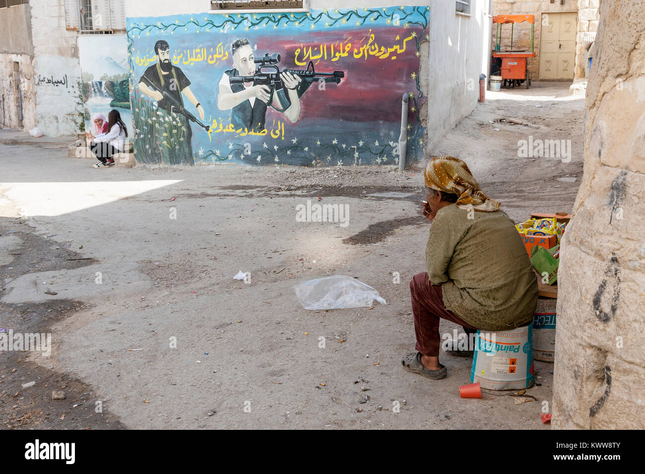 Jenin, Palestine, November 18, 2010: An old Palestinian woman is looking at a big graffiti of martyrs who fought with Israeli soldiers in Jenin refuge Stock Photo