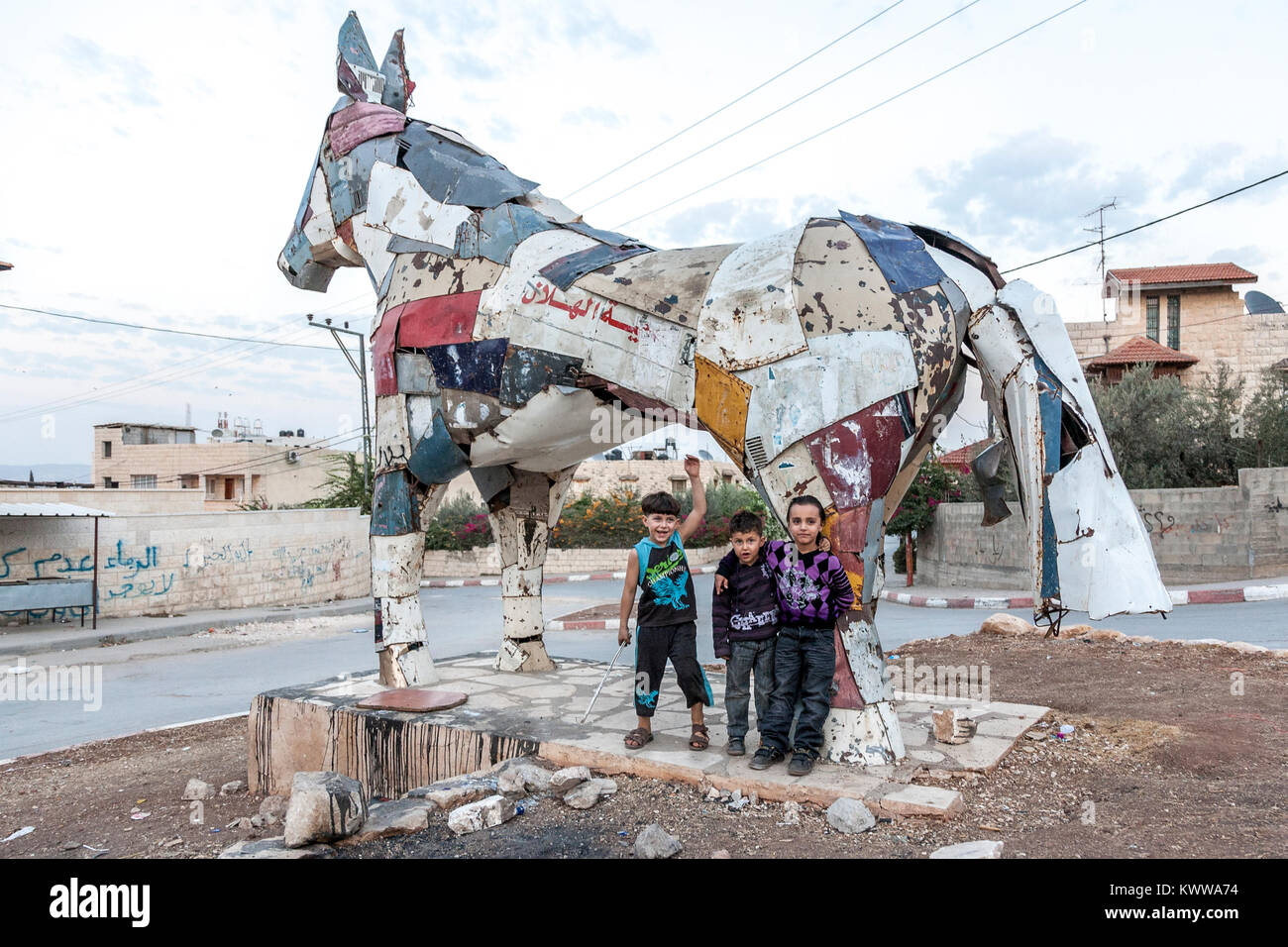 Jenin, Palestine, November 18, 2010: Palestinian children are standing in front of a horse built by German artist from car scrap metal crushed by Isra Stock Photo