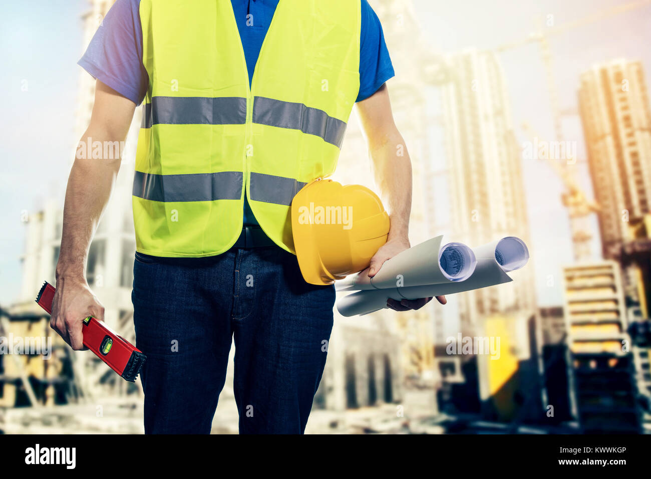 construction engineer with safety vest and blueprint rolls in hand at building site Stock Photo