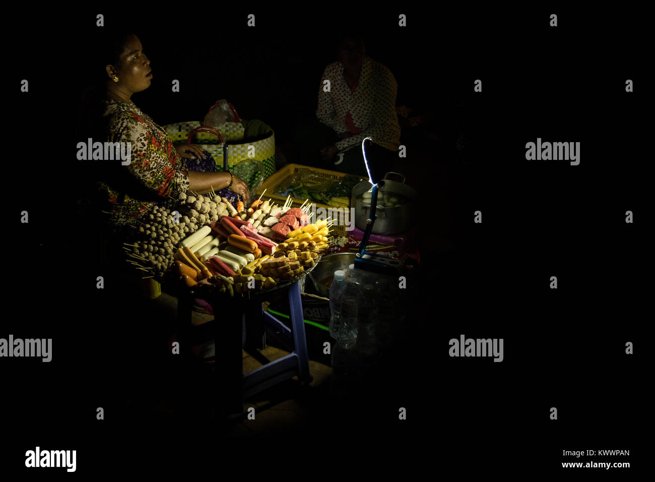 An Asian woman selling street food at night processed food, sausages