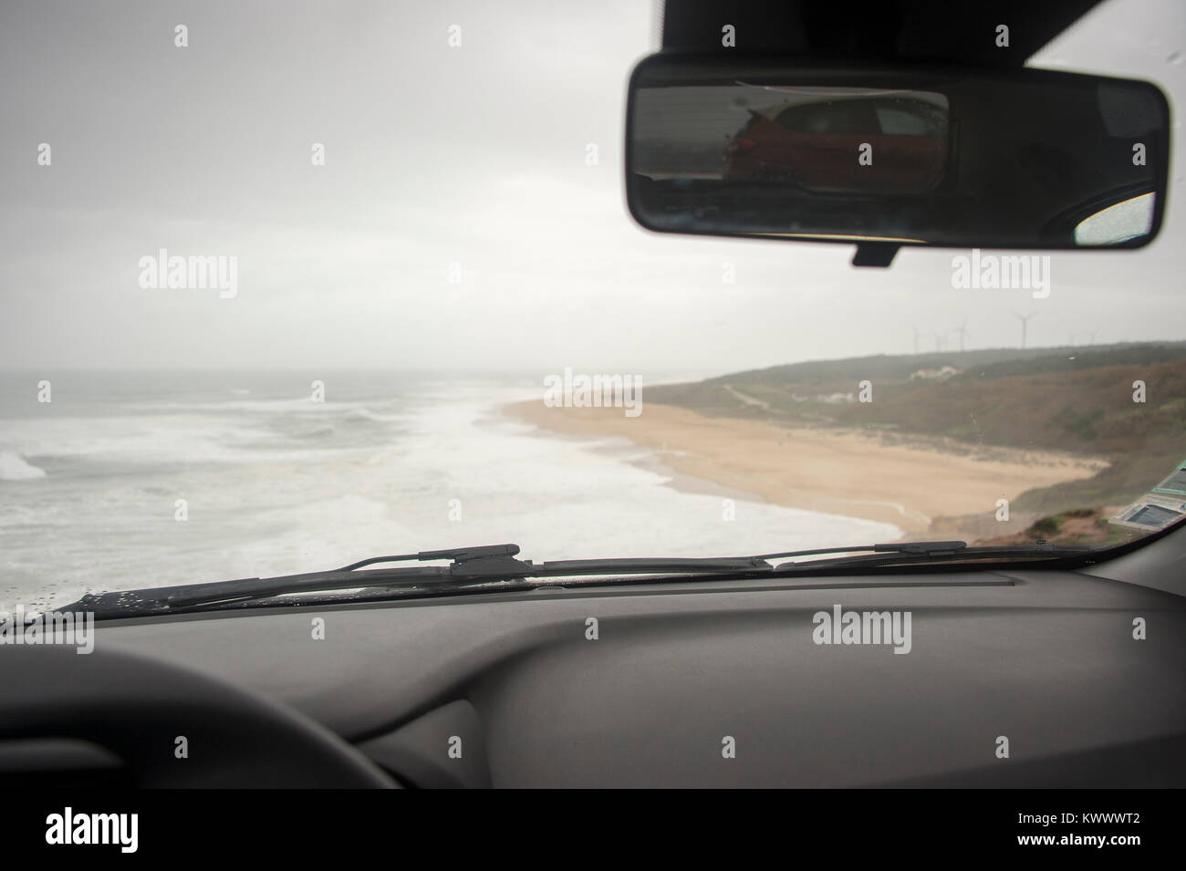 view form inside a parked car at the beach on a wet and windy day on holiday at praia do norte Portugal Stock Photo