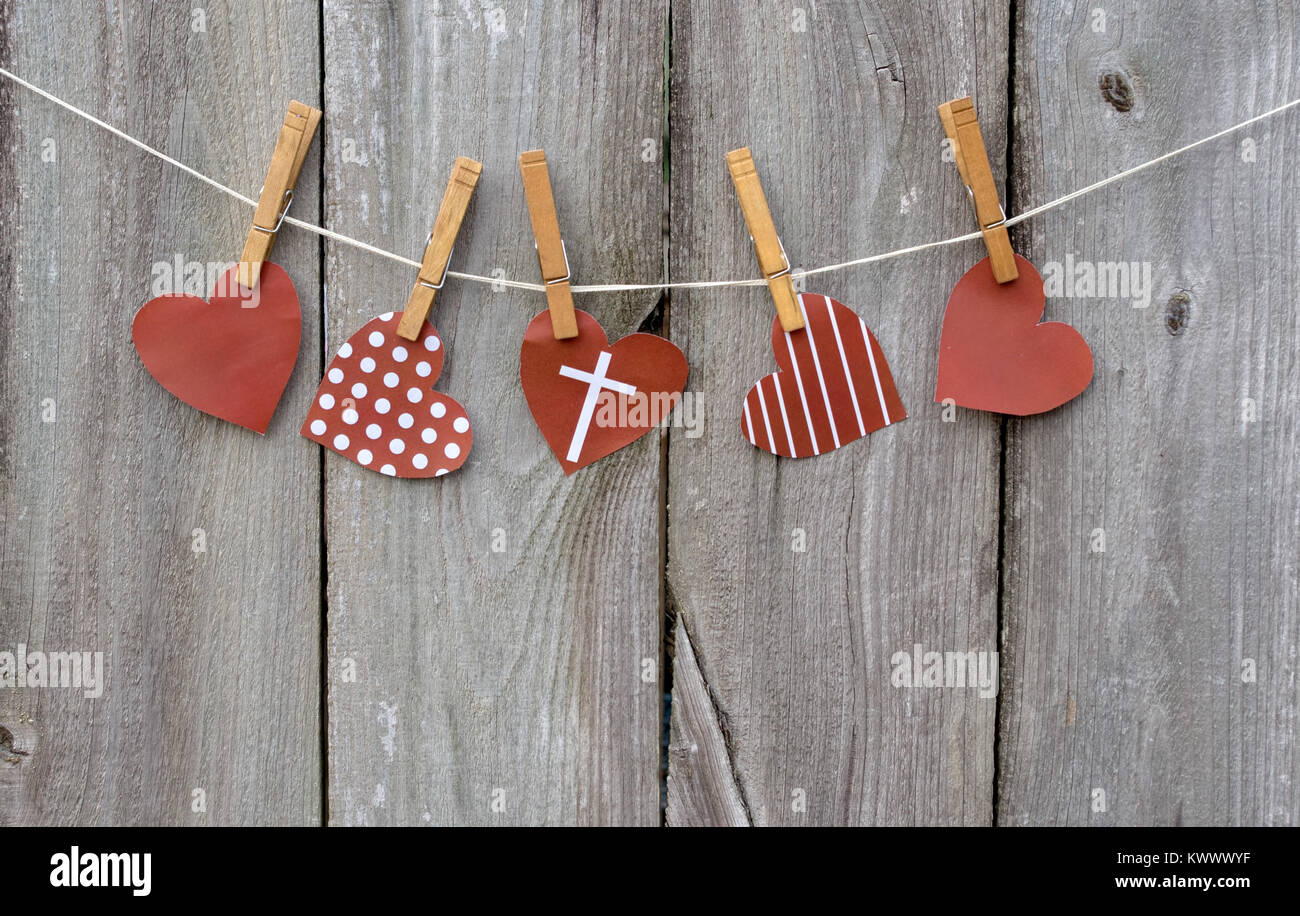 Red hearts with cross hanging from clothespins in front of distressed wooden fence Stock Photo