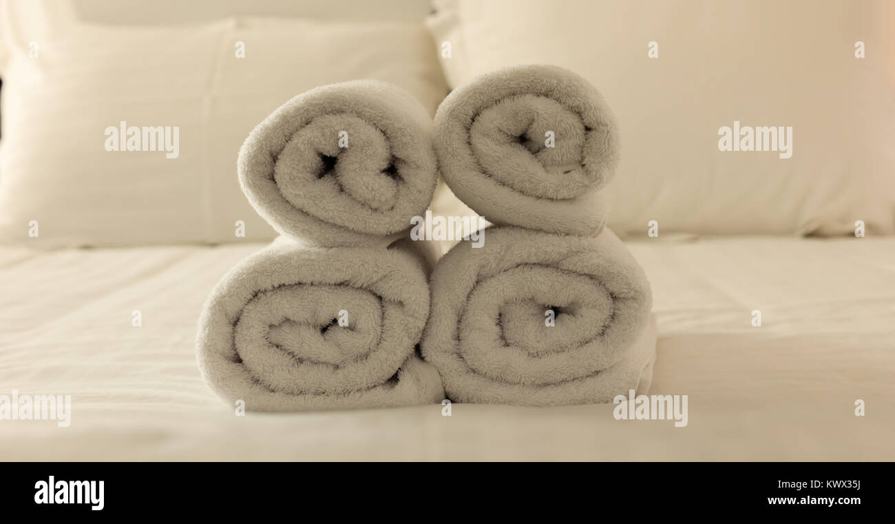 Hotel's bedroom. White fluffy, rolled towels, linen sheets and pillows on a tidy bed. Closeup. Stock Photo