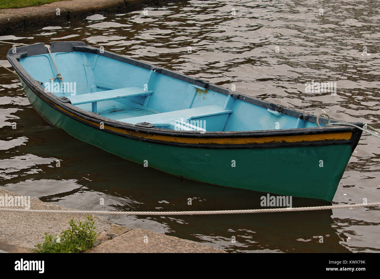 A green and blue rowing boat tied up on the side of a river. Stock Photo