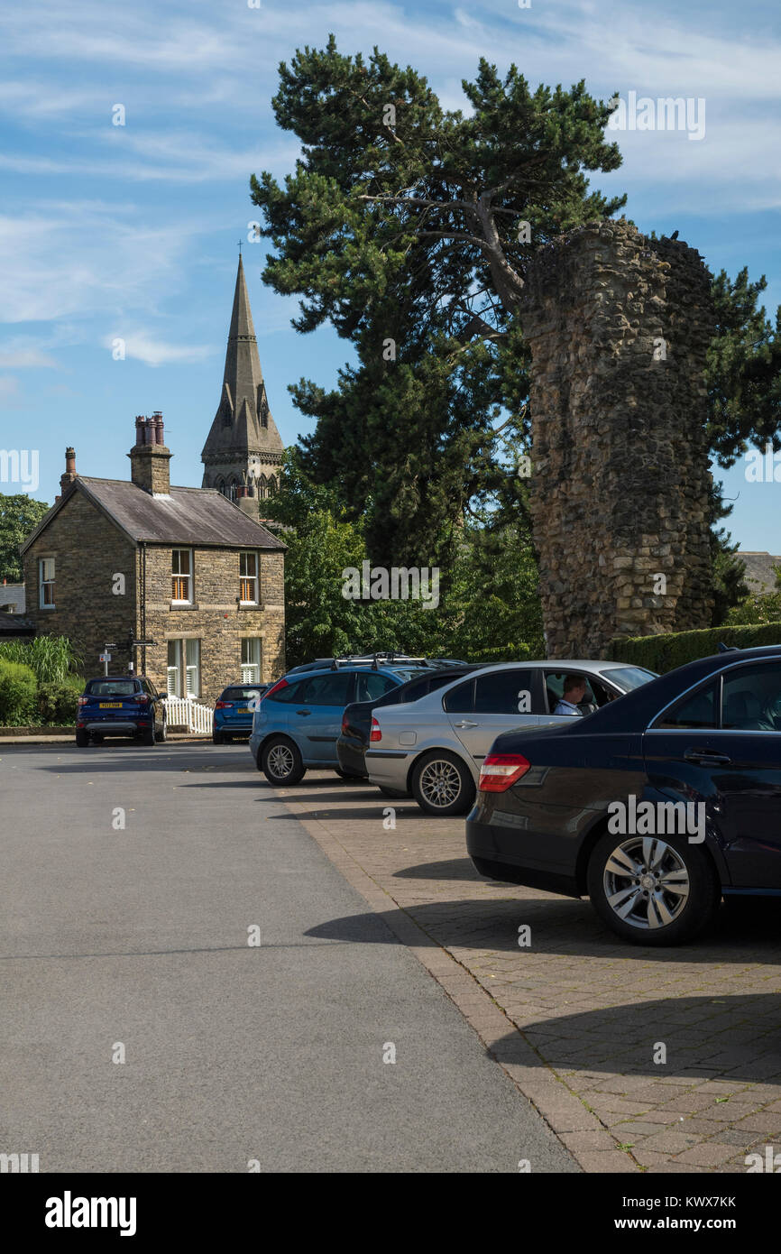 Cars parked in town centre car park by castle ruins on sunny summer day, with tall church spire beyond - Knaresborough, North Yorkshire, England, UK. Stock Photo