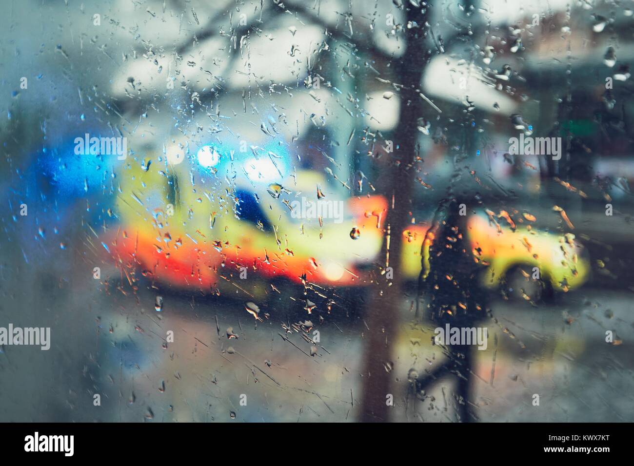 Emergency medical service response in the city. Ambulance cars on the rush street during rain. View through a car window and selective focus on the ra Stock Photo