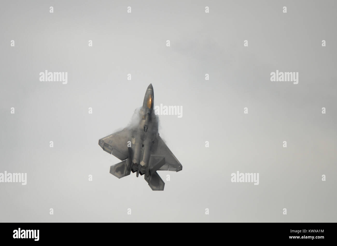 An F22 Raptor fighter jet climbs vertically. Cloud and condensation forms on the wings. Stock Photo