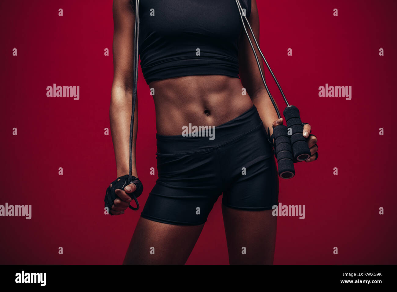 Woman with muscular abs holding jumping rope. Female fitness model with ...