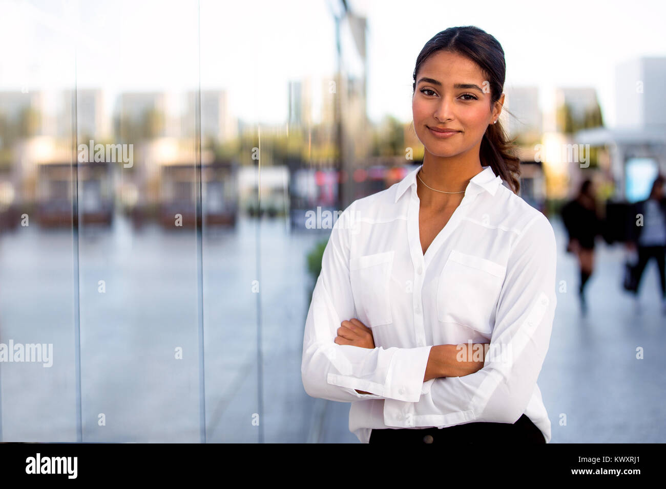 Beautiful female corporate executive modern business woman standing arms folded outside work at office building Stock Photo