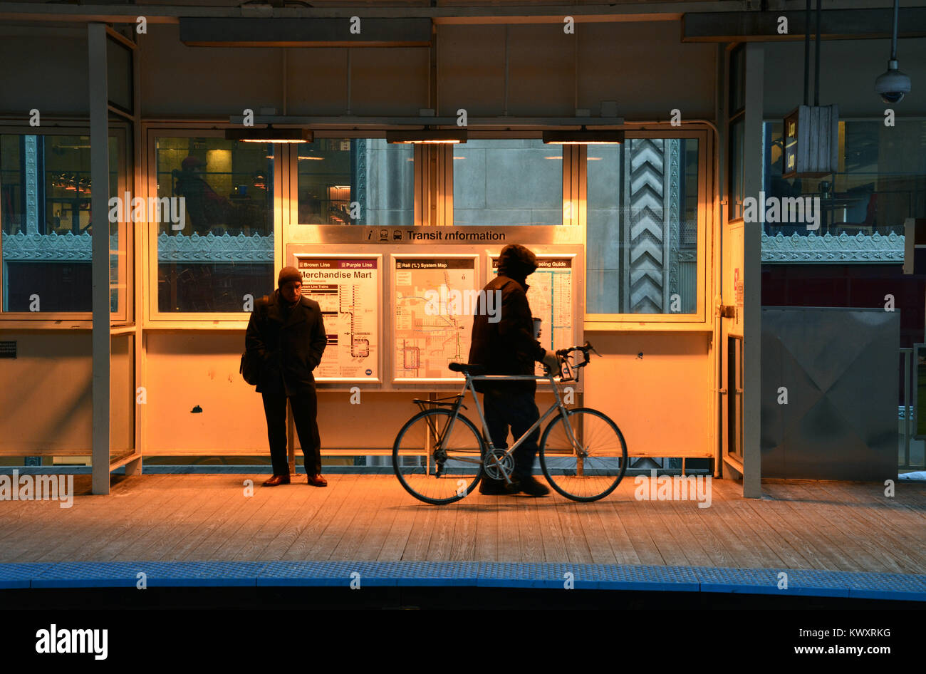 Two men stand under the heating shelter to keep warm in January while waiting for an inbound L train at the Merchandise Mart station in Chicago Stock Photo