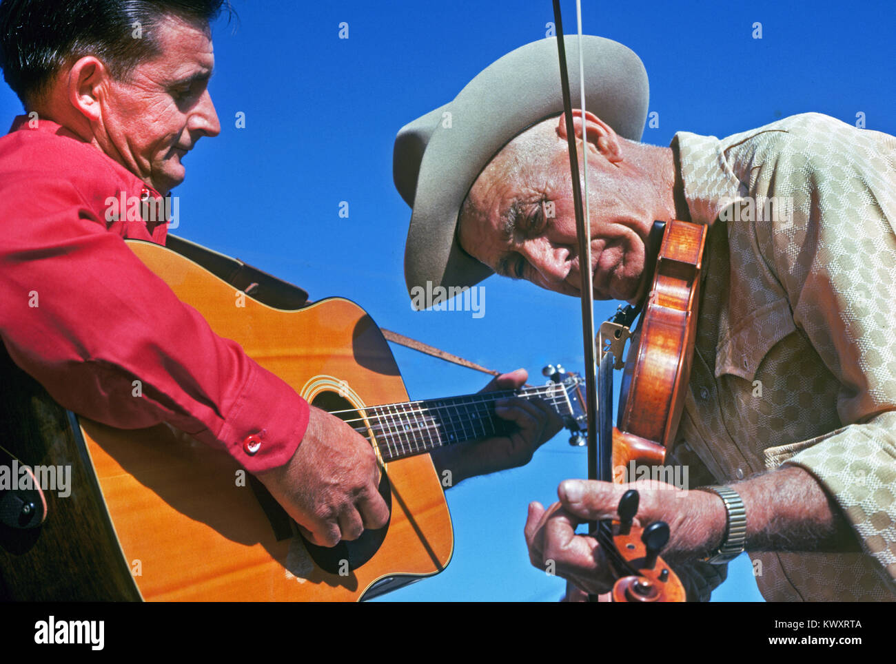 A man playing a fiddle or violin and a man playing an acoustic guitar