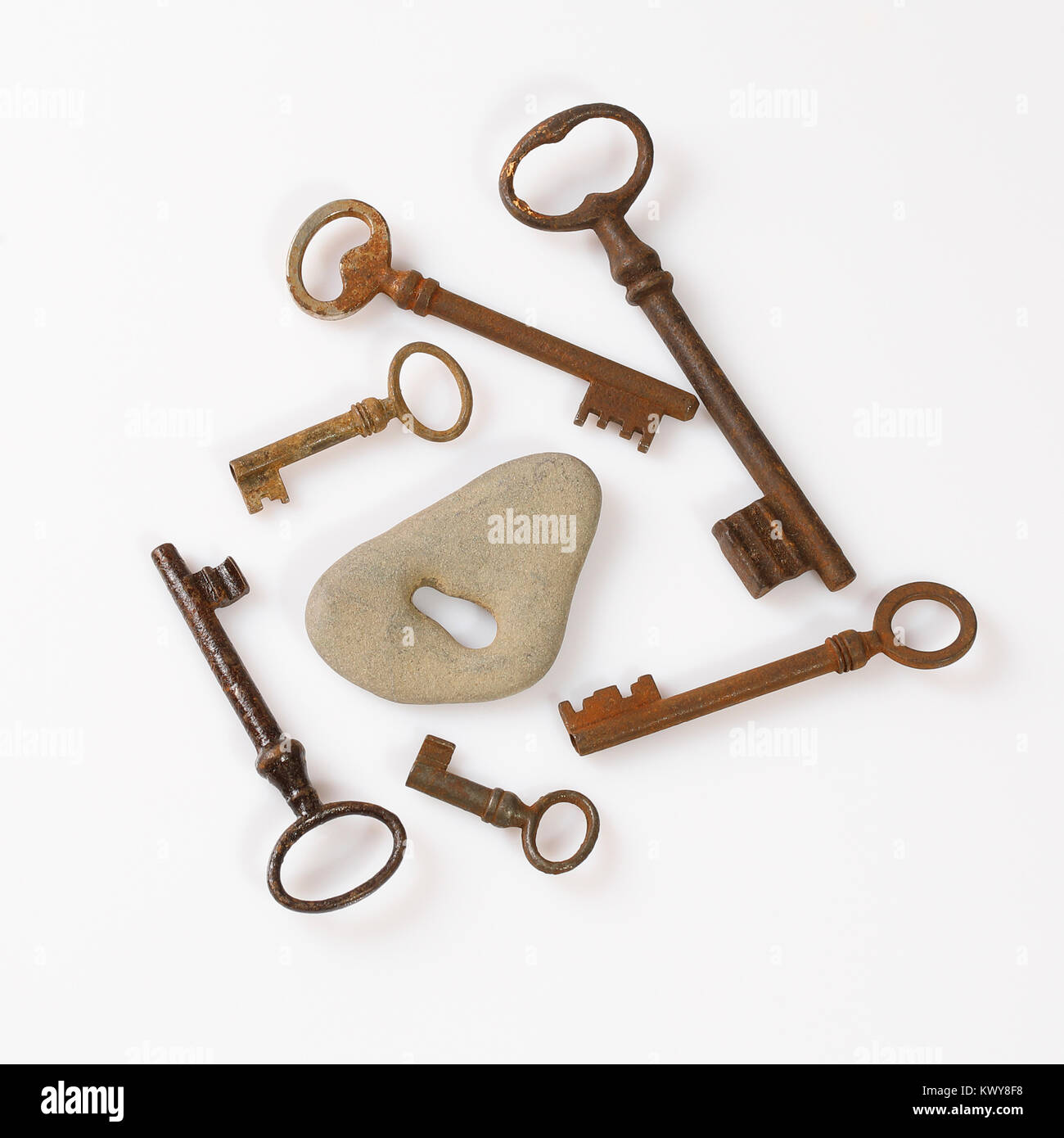 set of old rusty keys placed around grey stone with key hole on white background  - concept of choice Stock Photo