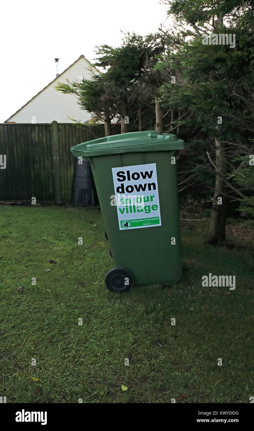 sign requesting drivers slow down in village, posted on wheelie bin