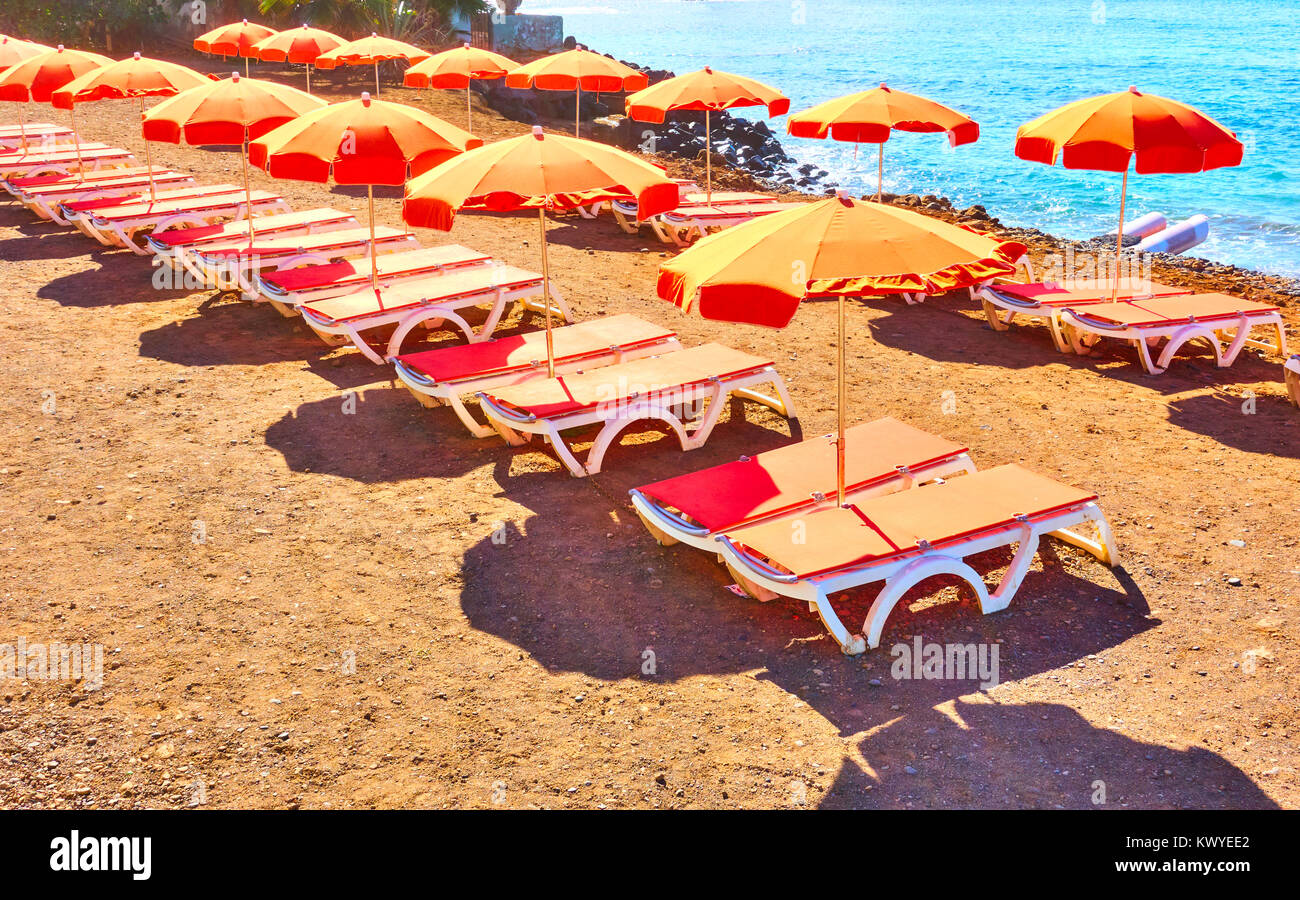 Orange umbrellas and chaise-longues on a sea beach, Tenerife Stock Photo
