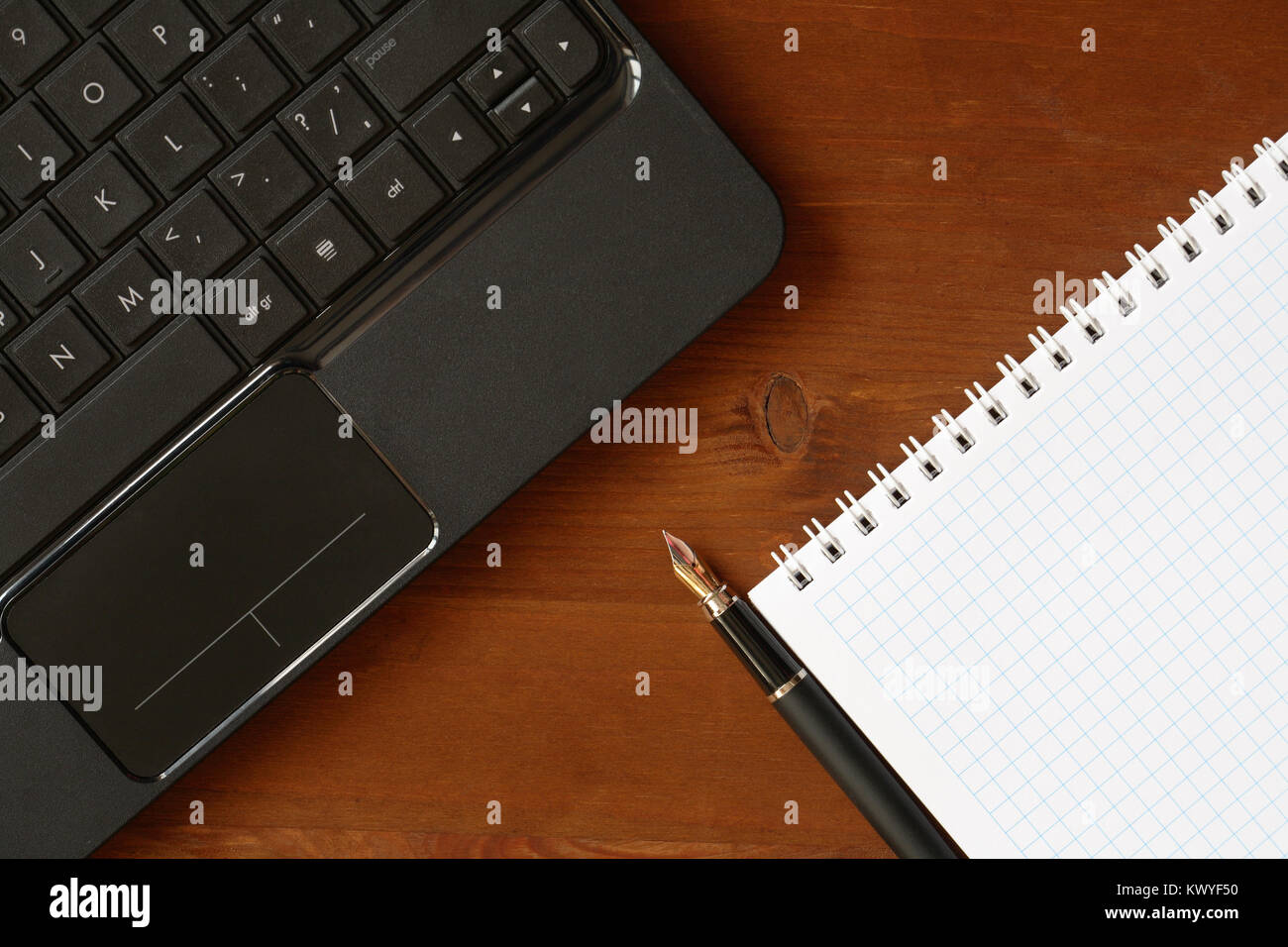 Closeup of blank spiral notebook and pen near black laptop on wooden