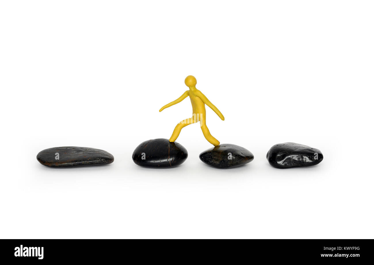 Yellow plasticine man walking on black stones. Isolated on white with clipping path Stock Photo