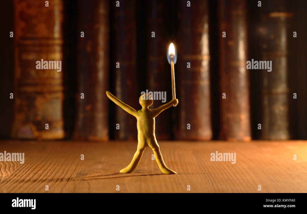 Small yellow plasticine man with lighting match standing in front of old books Stock Photo