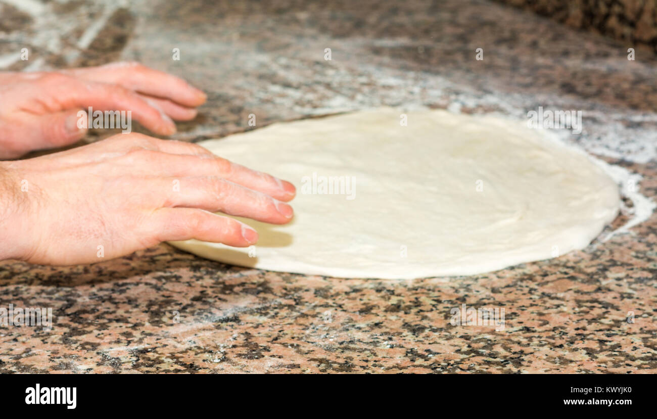 the chef's hands knead the dough to make pizza in the kitchen. Food, italian cuisine and cooking concept. Preparation of the Italian Pizza. Stock Photo