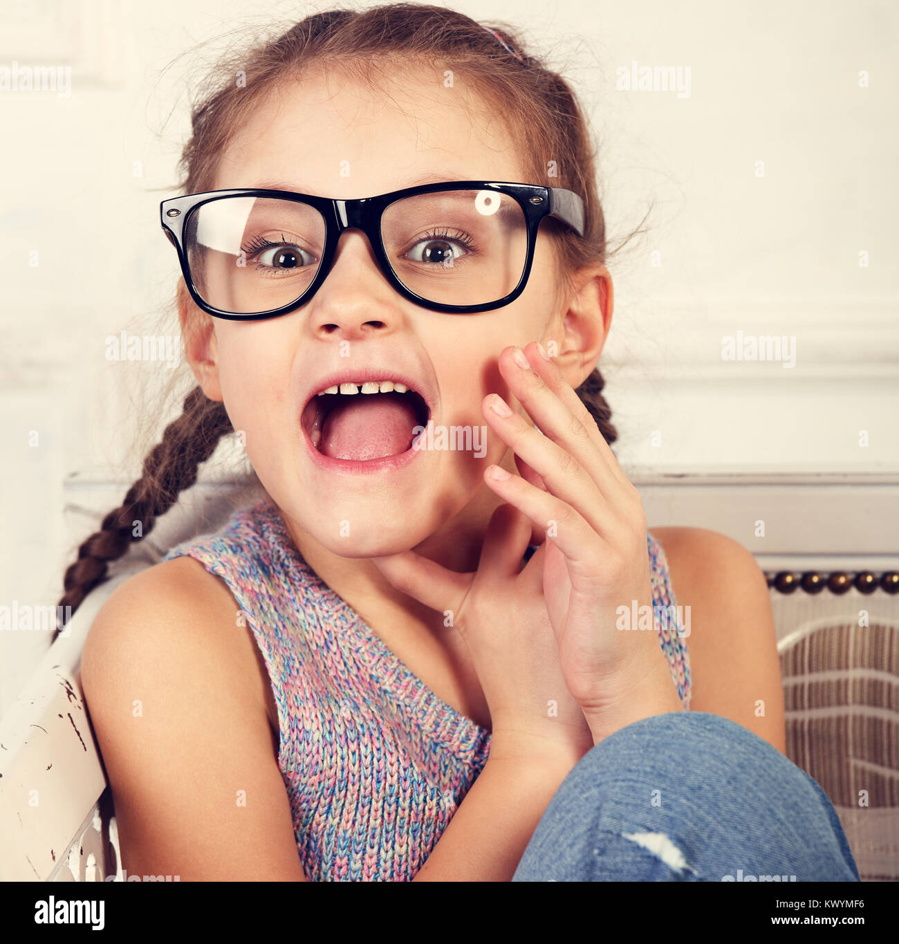 Happy excited surprising kid girl in fashion eyeglasses looking with open mouth. Closeup toned vintage portrait Stock Photo