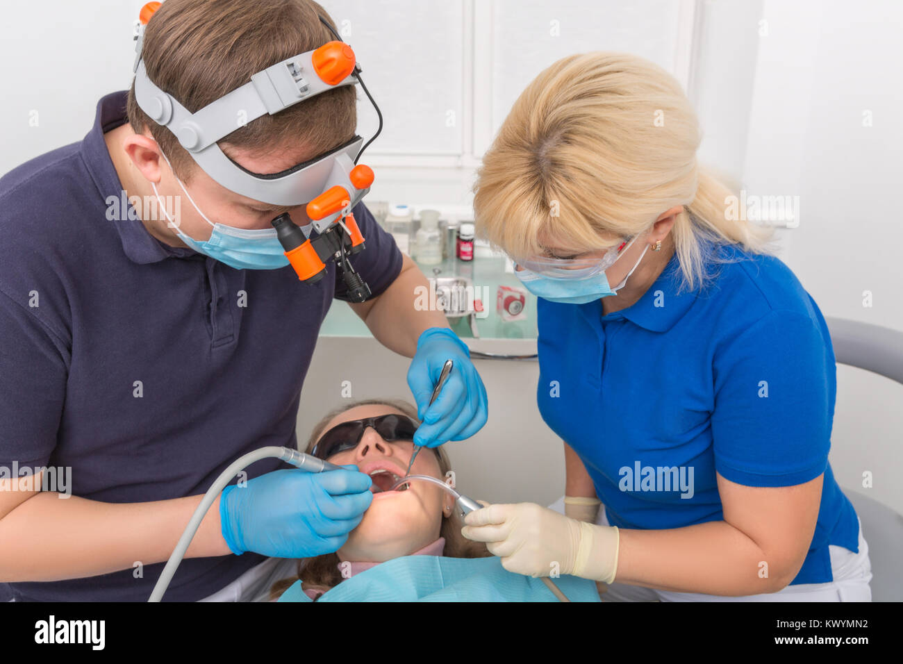 Dentist in mask with loupe binoculars and assistant working on patient. Madical office Stock Photo