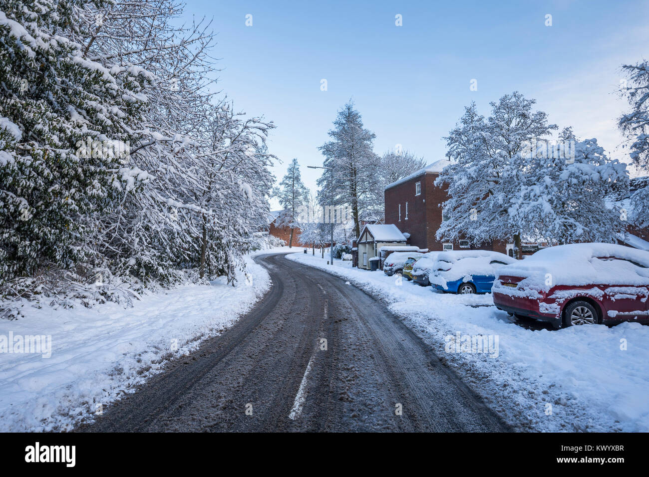 Empty asphalt road across residential area in United Kngdom with cars and trees covered in snow Stock Photo