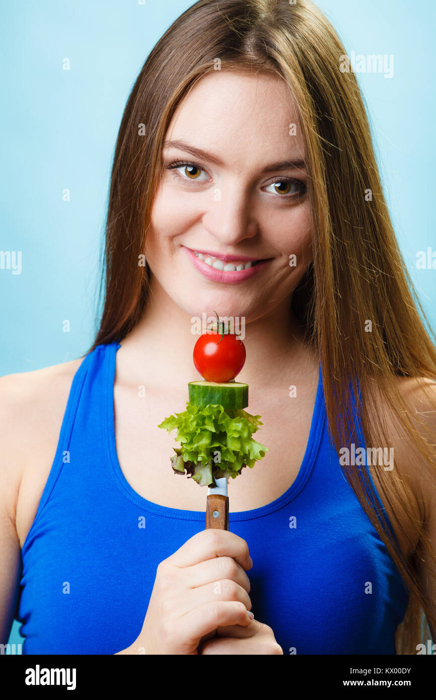 Vegetarian girl. Diet concept. Fit woman holding stack of vegetables on blue background in