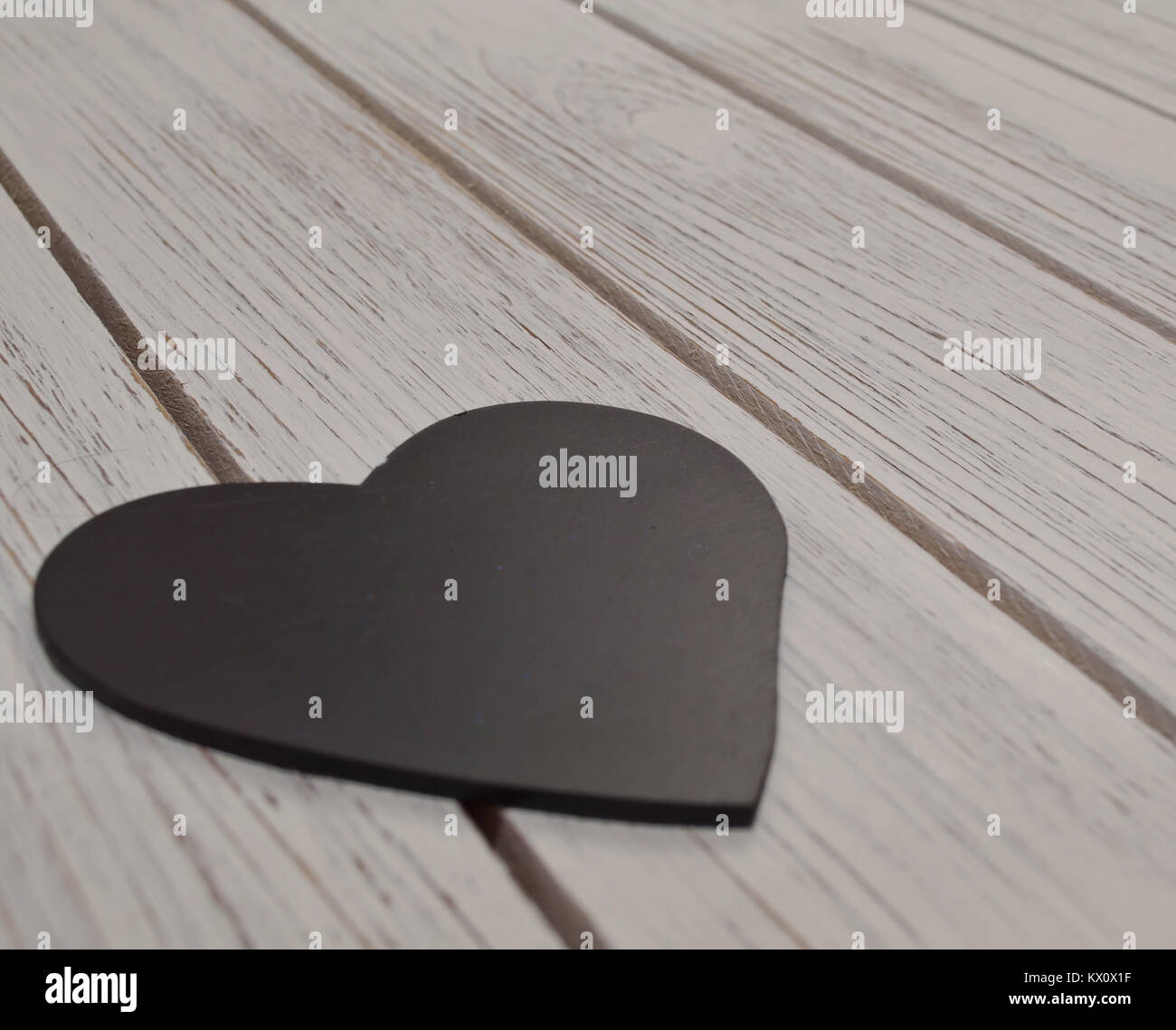 A black heart laying on a white wooden table Stock Photo