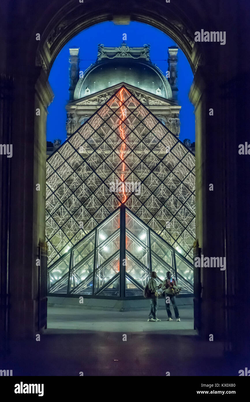 France, Paris (75), Louvre Museum at night with Pyramid illuminated. Two African tchotchke sellers. Stock Photo