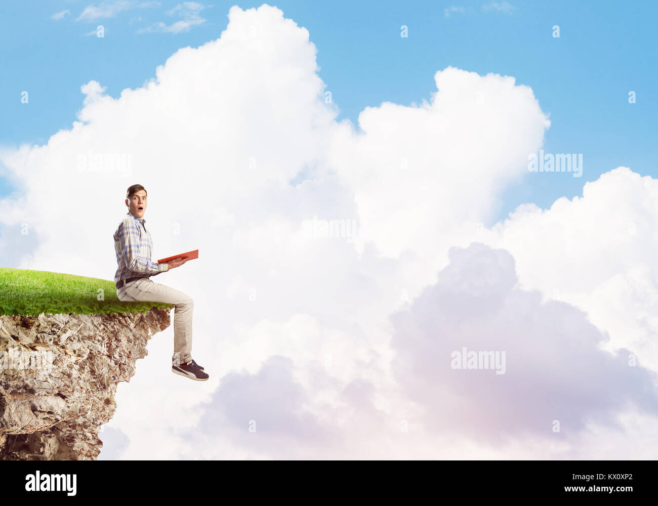 Young shocked man in casual sitting on green island with red book in hands Stock Photo