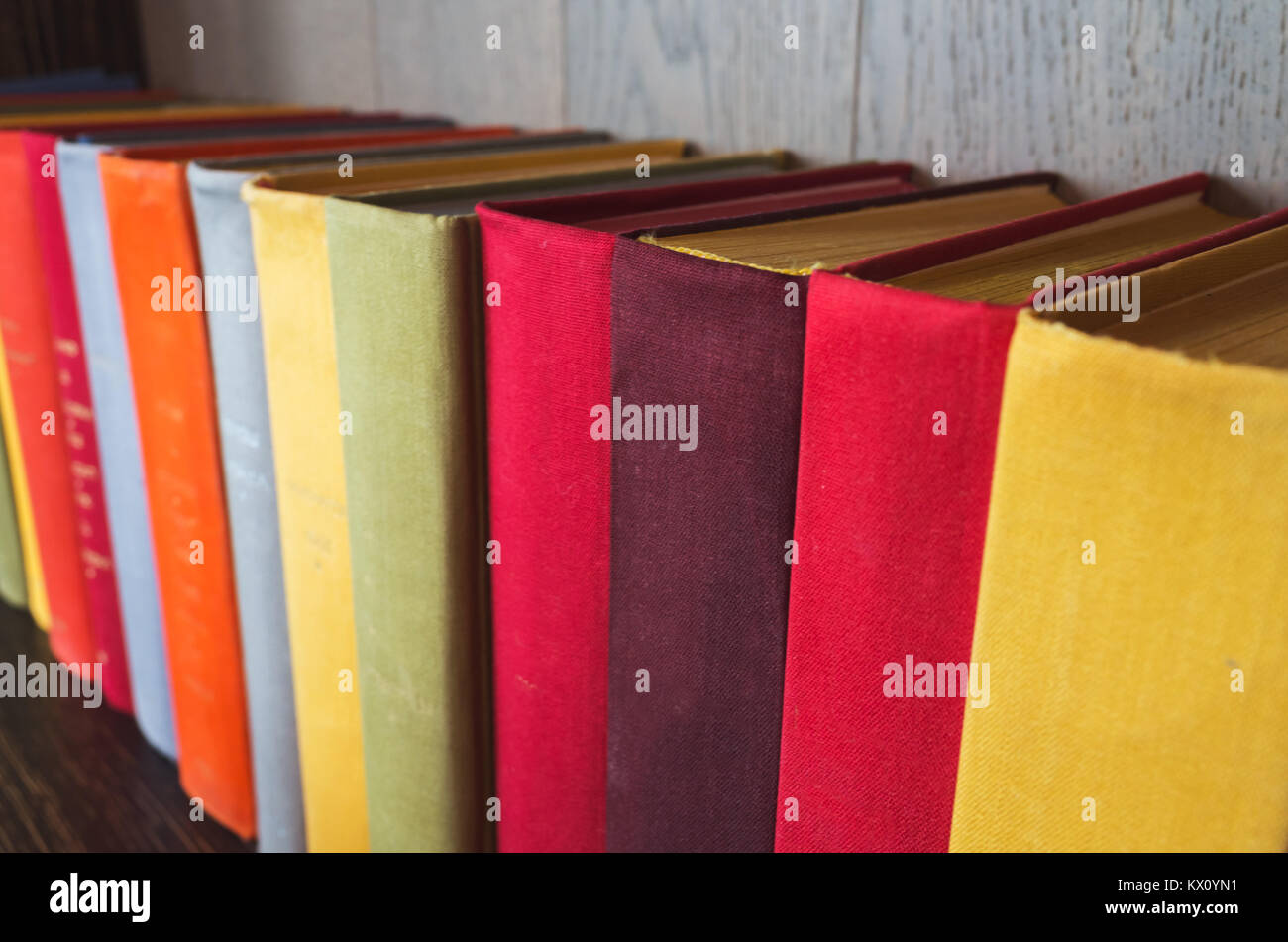Colorful old books stand in a row on wooden shelf Stock Photo