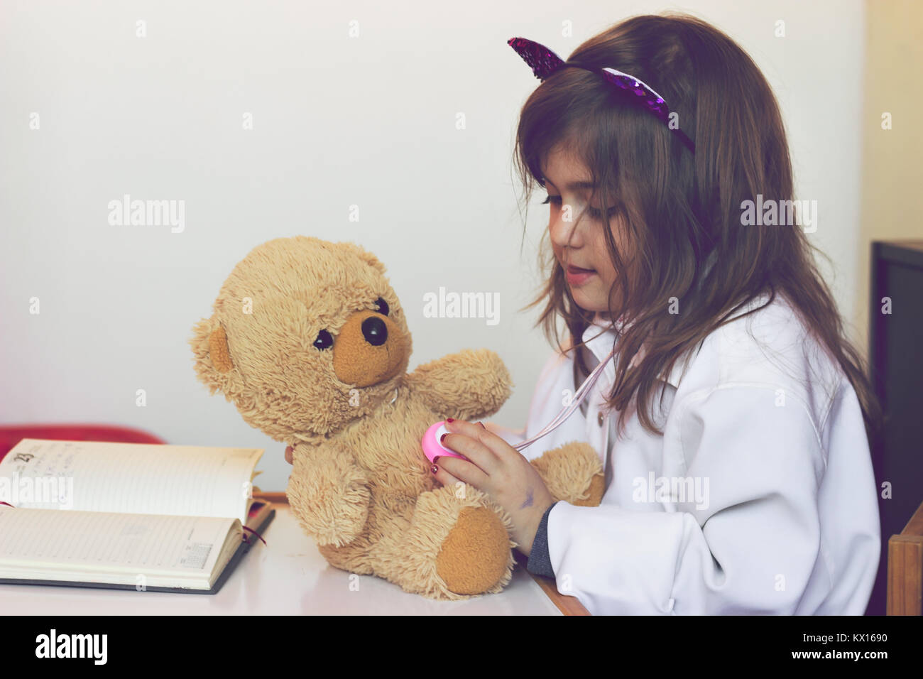 Little girl pretends to be a doctor and playing with her teddy bear Stock Photo