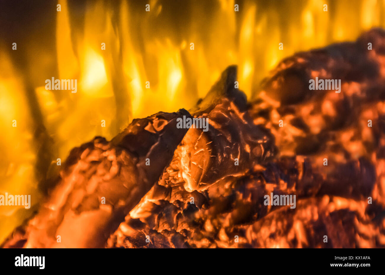 logs glowing and burning with golden flames in a glass fronted imitation electric wall log fire, fireplace. Background image for fire and warmth Stock Photo