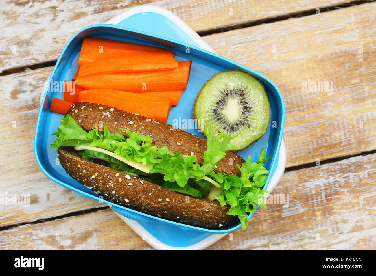 Healthy lunch box containing brown cheese sandwich, crunchy carrots and kiwi fruit Stock Photo
