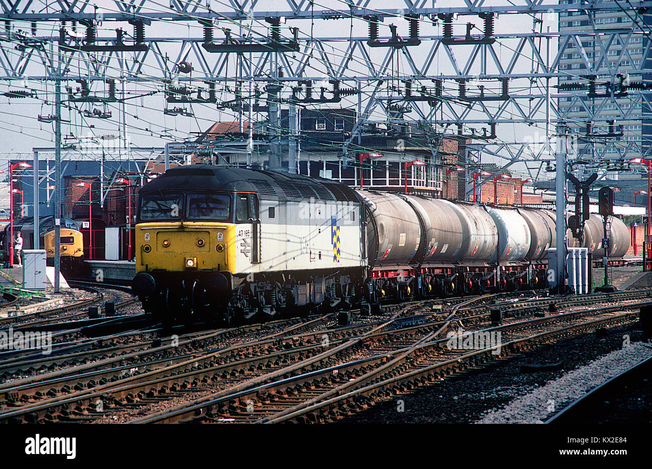 47195 hauls a short rake of two axle oil tanks from the Thameshaven oil refinery through Stratford while in the background 37140 awaits a path. 14th August 1991. Stock Photo