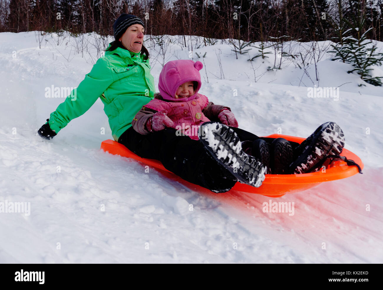 An adult woman in a sledge with a little girl (3 yr old) looking nervous as its much faster than she thought Stock Photo