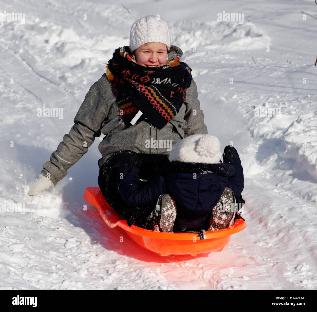 A smiling young mother sledging with her infant (1 yr old) daughter Stock Photo