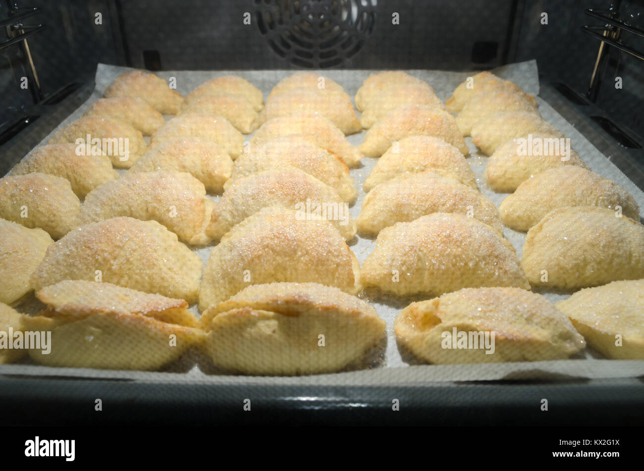 Set of homemade sweet yeast croissants covered in sugar crystals and filled with apples, during baking inside home bakery oven. Stock Photo