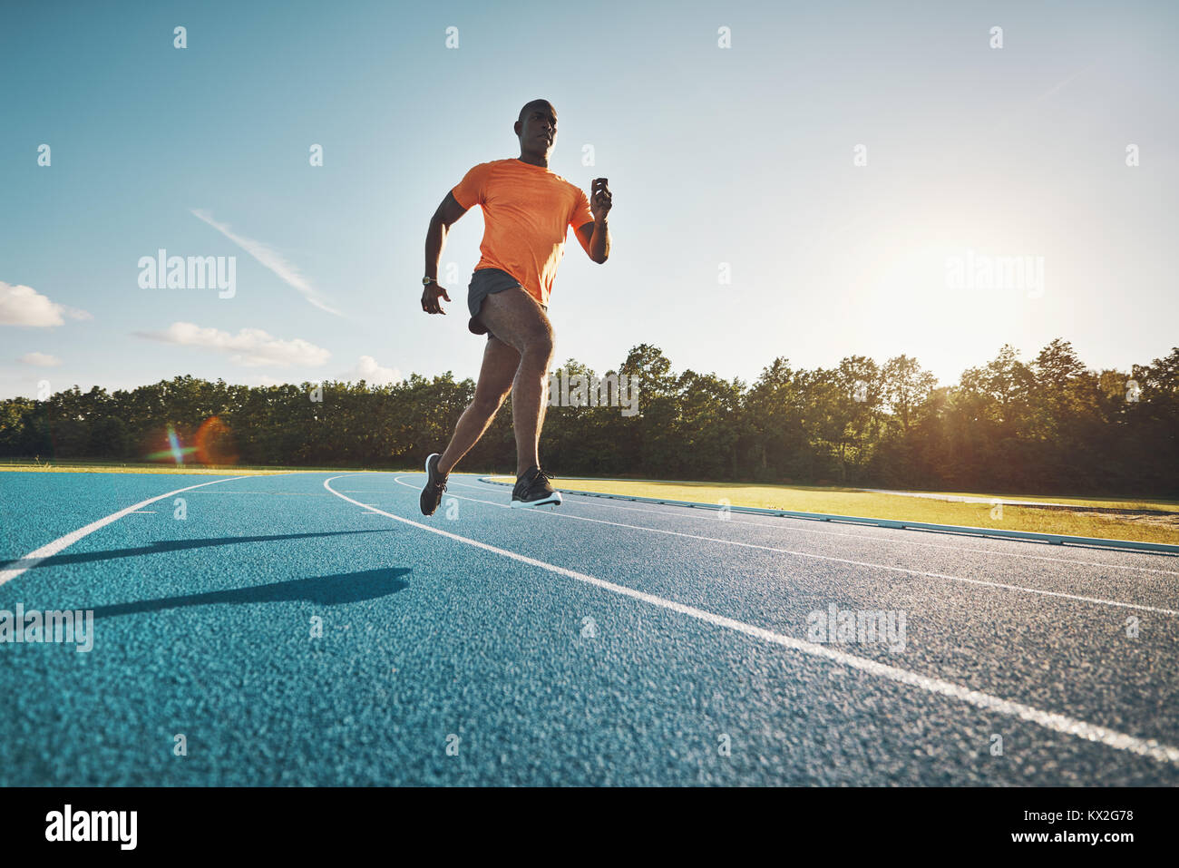 Focused young African runner in sportswear racing alone down a running track on a sunny day Stock Photo