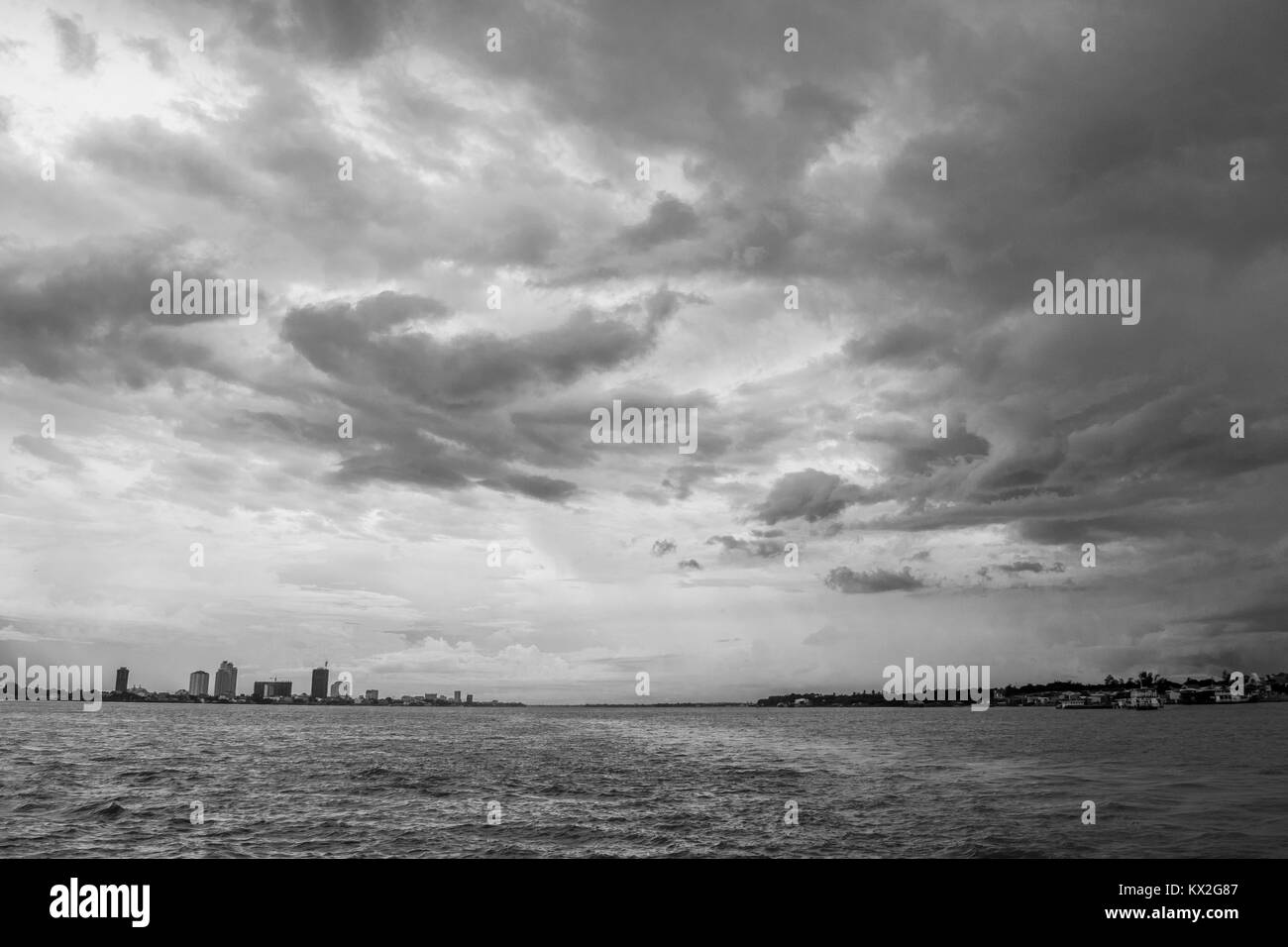 Where the Mekong meets Tonle Sap, river banks in Phnom Penh Cambodia, South East Asia, brown river water, grey thick cloud cover of monsoon season. Stock Photo