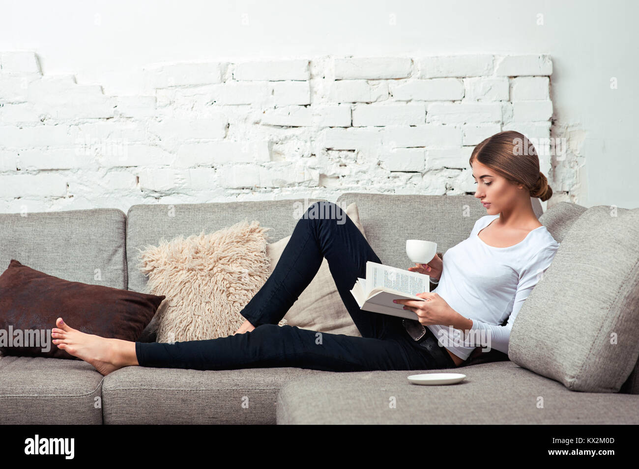 Young beautiful woman sitting on the sofa reading a book holding her
