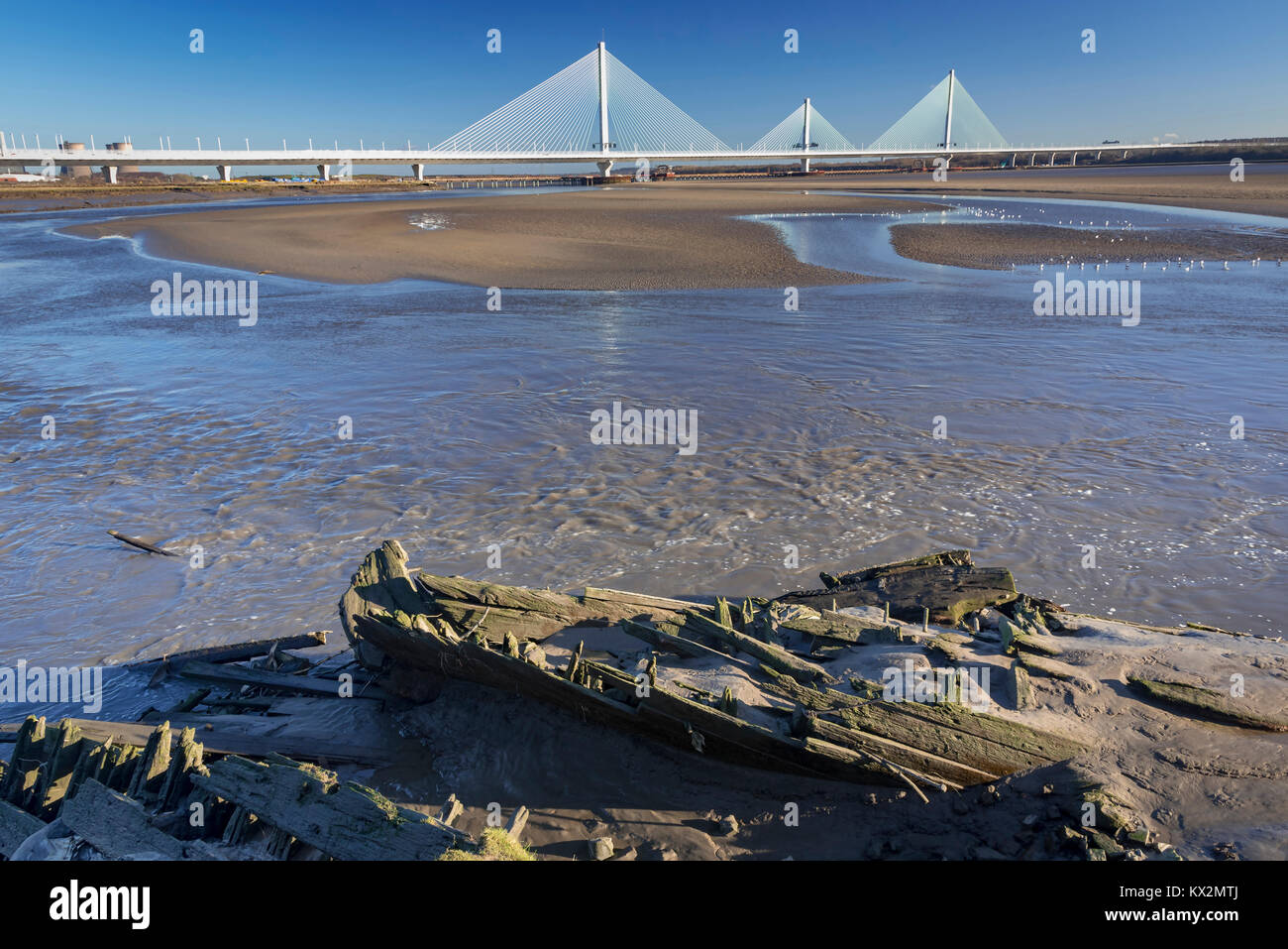 Gateway bridge over the river Mersey seen from Widnes to Runcorn with wrecked wooden boat in the mud. Stock Photo