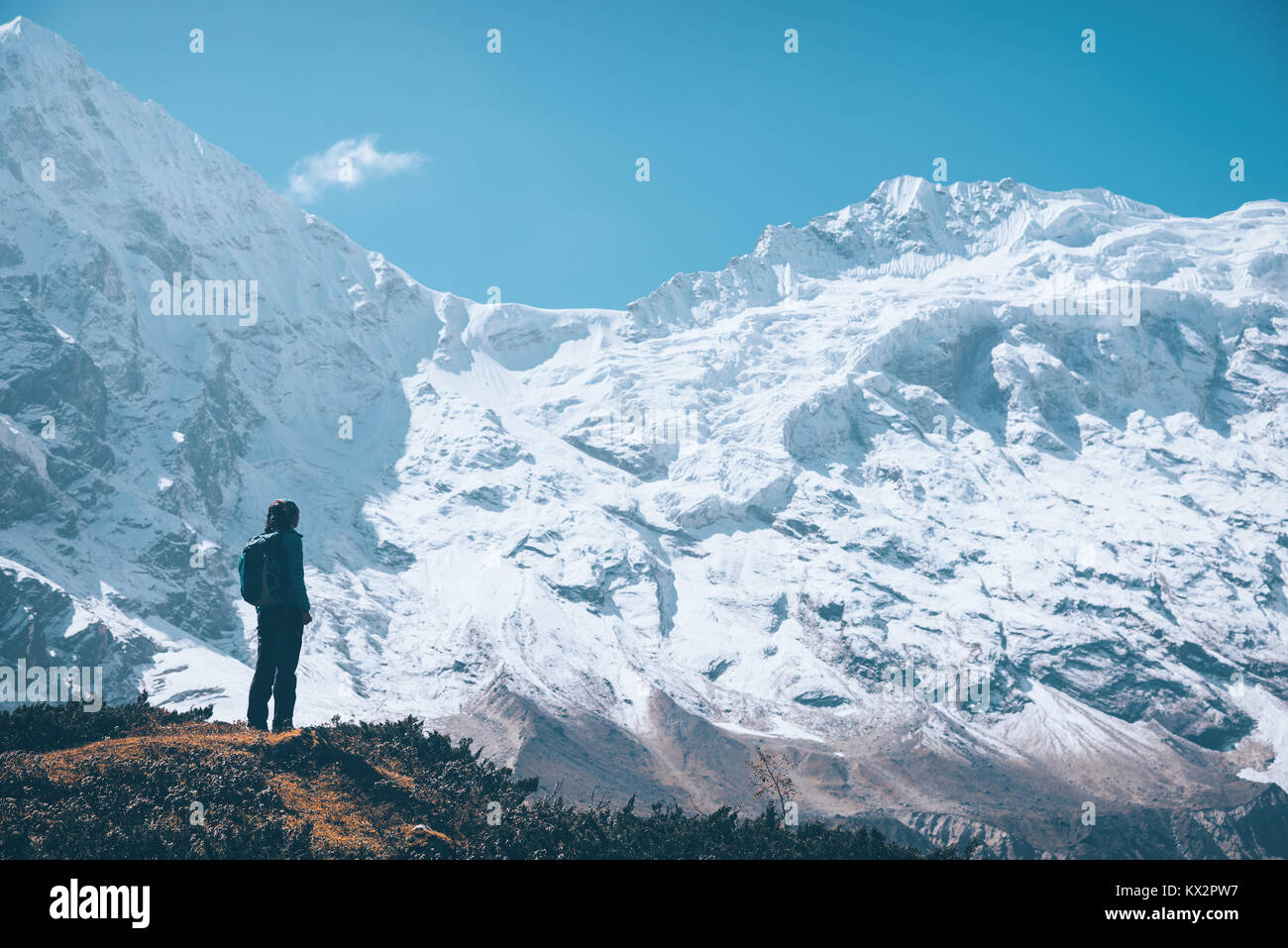 Standing young woman on the mountain trail and looking on snow covered rocks at sunset. Landscape with girl, high mountains with snowy peaks, path, bl Stock Photo