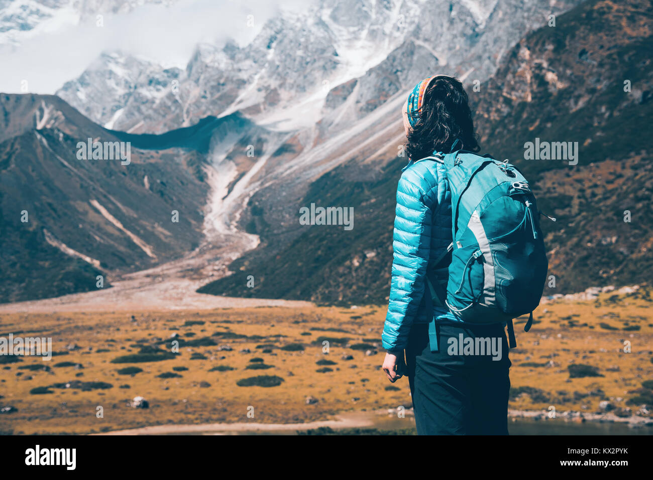 Woman with backpack looking on beautiful mountains in clouds at sunrise. Landscape with girl, high rocks with snowy peaks, blue sky with clouds in Nep Stock Photo