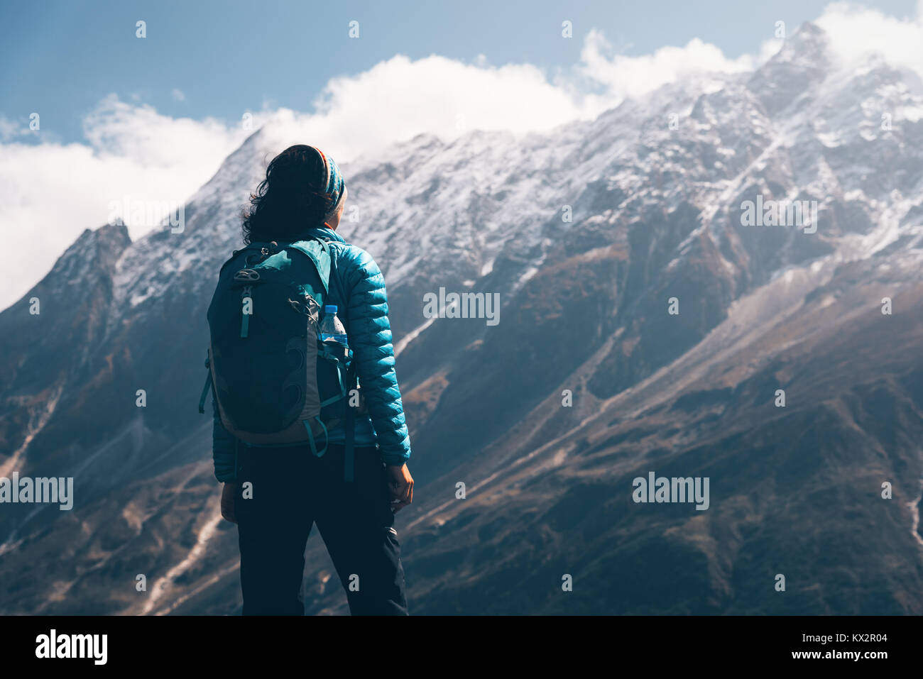 Woman with backpack looking on beautiful mountains in clouds at sunrise. Landscape with girl, high rocks with snowy peaks, blue sky with clouds in Nep Stock Photo